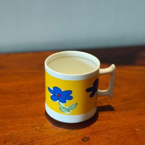 Yellow coffee cup with blue flower sitting on a table.