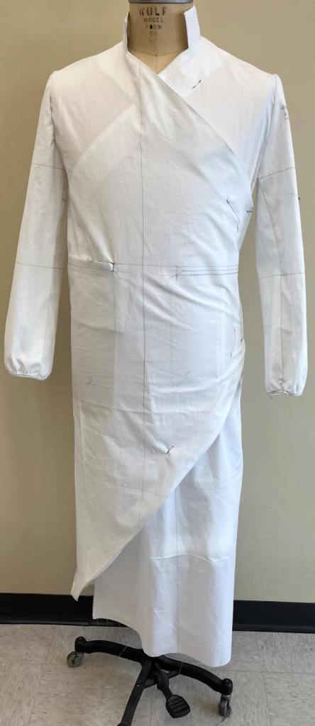 A white garment draped on a dress form, showcasing an unfinished design with pinned fabric and a modern silhouette.