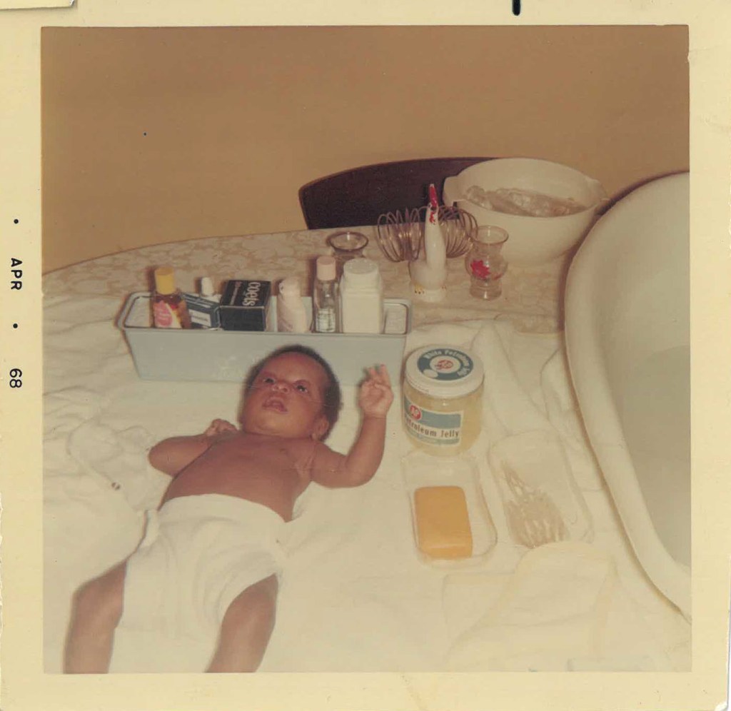 Faded photo of Baby Shari laying down with care products for diaper change.