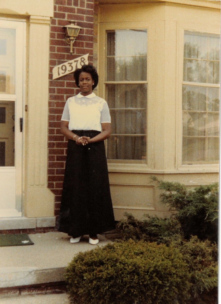 High school Shari standing on her front step of home in Detroit, MI in choir outfit.